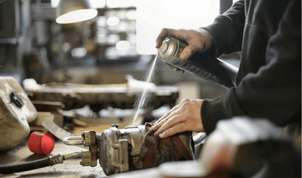 Hands spraying a machine part